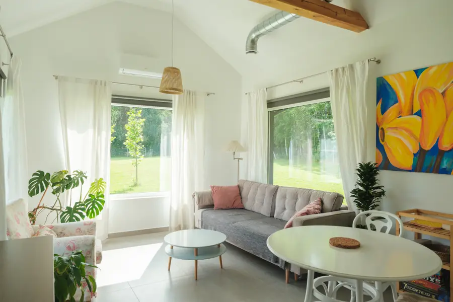 The living room, with a sofa, dining table and windows onto the grass and forest